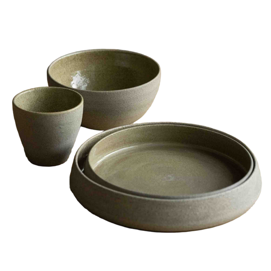 Set of ceramic bowls and a plate on a wooden table with a chair in the background.